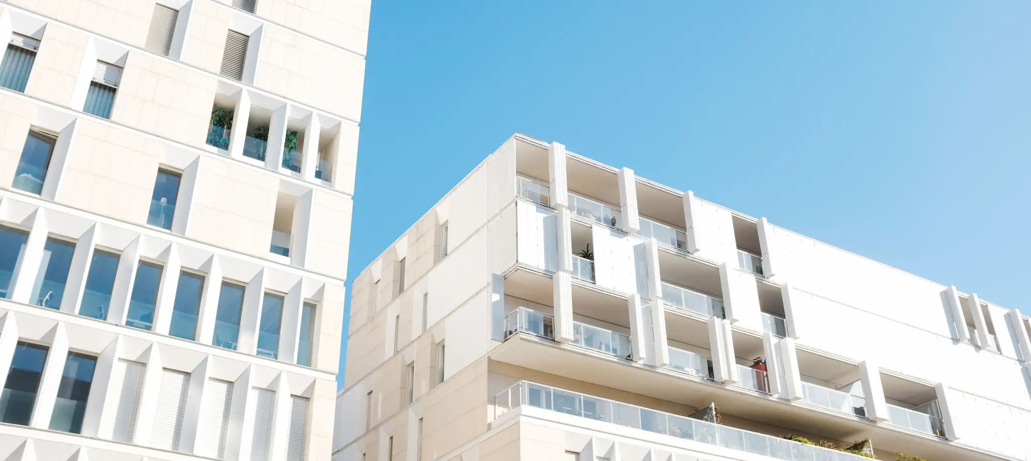 Looking up at the white balconied facades of modern apartment buildings